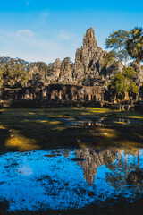 Fototapeta na wymiar Face off. Angkor Thom ancient city in the early morning light. Heavy rain the night before formed a lake around the main ruins reflecting the old stone structure.