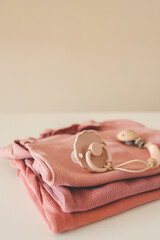 Stack of pink baby clothes and baby pacifier on beige background