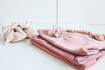 Stack of pink baby clothes and baby pacifier on white background
