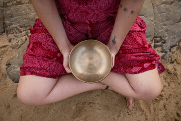 Mujer sosteniendo cuenco tibetano entre sus piernas semidesnudas en la playa