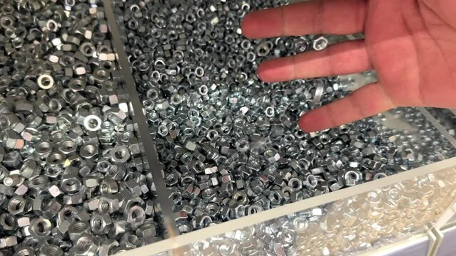 Hand in a Box of new shiny Stainless Steel Hex Locking Nuts in Hardware store, close-up