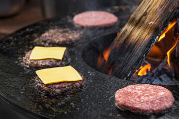 Large piece of meat burger being grilled with flames.