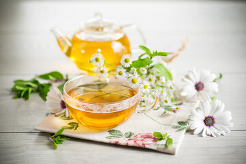 Chamomile flower tea in a glass cup and teapot, on a wooden table.