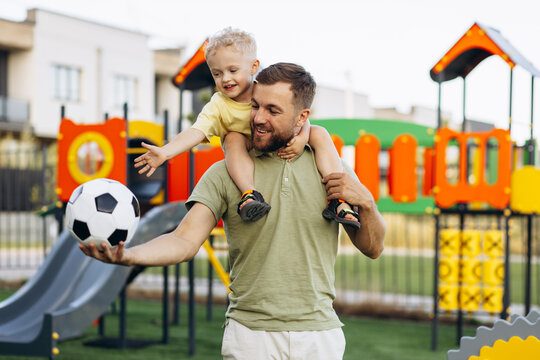 Father with son holding football ball and having fun at the playground