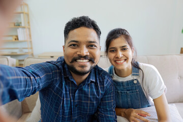 Indian couple taking selfie photo or video call while sitting on the couch at home