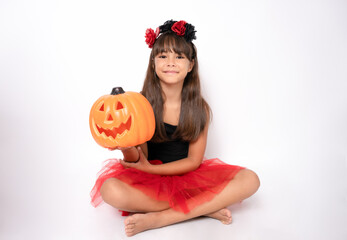 Cute little girl lying on floor in halloween costume holding a pumpkin isolated over white background.