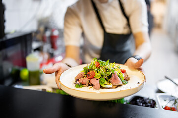 Chef cooking woman salad with fresh vegetables and meat on restaurant kitchen