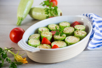 Raw zucchini with tomatoes prepared for baking in a ceramic form.