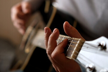 Playing the guitar. Strumming acoustic guitar. Musician plays music. Man fingers holding mediator. Man hand playing guitar neck in dark room. Unrecognizable person rehearsing, fretboard close-up