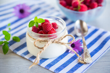 Sweet cooked homemade yogurt with fresh raspberries in a glass jar.