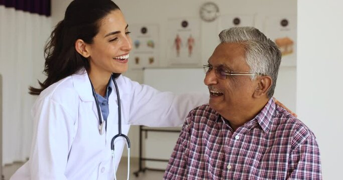 Smiling female therapist, medical worker hug happy older patient, encouraging, giving hope share optimistic news about recovery, enjoy pleasant conversation at visit in clinic. Eldercare, gerontology
