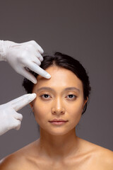 Hands of beautician in white surgical gloves touching face of asian woman with dark hair, copy space