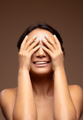 Smling asian woman with dark hair wearing blue nail varnish with hands over eyes