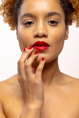Biracial woman with curly hair wearing red lipstick and nail varnish touching chin