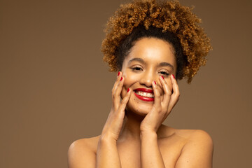 Happy biracial woman wearing red lipstick and nail varnish touching face with hands, copy space