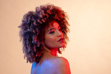Biracial woman with curly hair wearing pink eyeshadow and lipstick in red and blue light, copy space