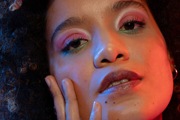 Close up of biracial woman with curly hair wearing eyeshadow and lipstick touching face