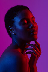 African american woman touching chin with eyes closed in red light on purple background