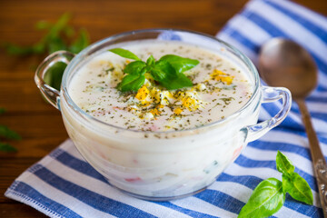 Cold soup with cucumbers, eggs, vegetables, yogurt and fresh herbs in a glass bowl .