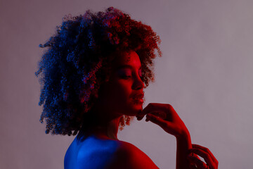 Biracial woman with curly hair touching chin in blue and red light