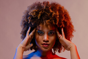 Biracial woman with curly hair touching temples in blue and red light