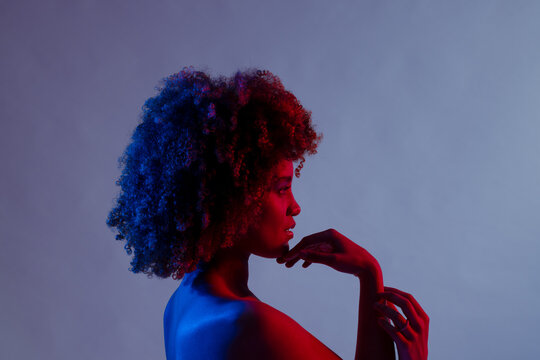 Profile of biracial woman with curly hair touching chin in blue and red light