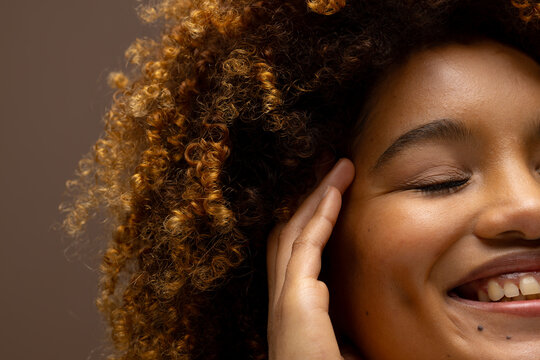 Smiling biracial woman with curly hair touching face with eyes closed