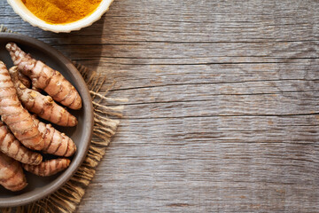 Fresh turmeric root with dry curcuma powder on wooden background with copy space