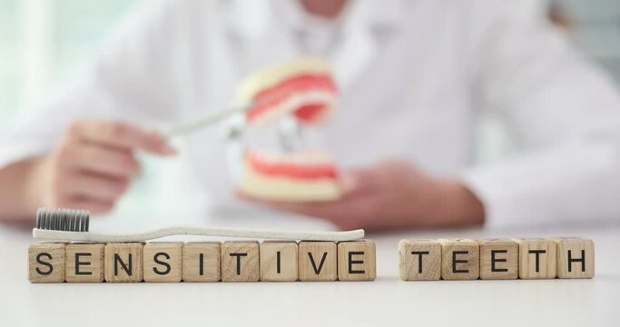 Dentist cleans teeth of artificial jaw model and word text sensitive teeth. Oral hygiene