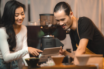 Asian Cashier is making order on touch screen of computer in cafe or store. Barista is using the screen to receive orders from customers who are pointing to order coffee.