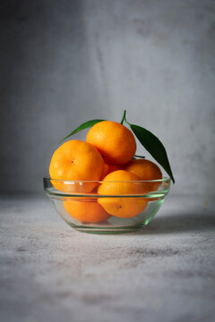 Fresh orange fruits with leaves in glass bowl. mandarin orange on grey and texture background 