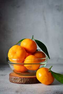 bunch of fresh orange fruits in a glass bowl. mandarin orange on grey and texture background 