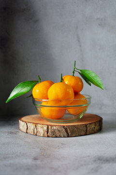 bunch of orange fruits with leaves in a glass bowl. mandarin orange fruits on grey and texture background 