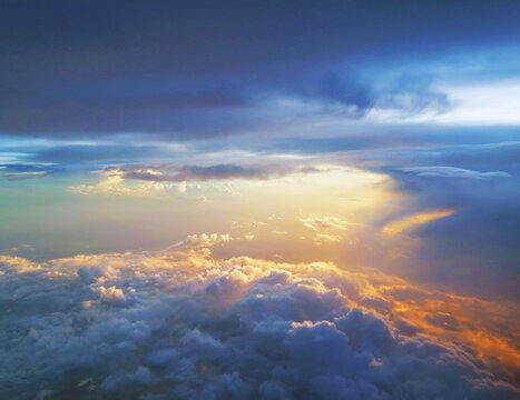 Stunning arial view of Golden sunrays and rays of sunlight over the clouds on the blue sky background looking out of aircraft window. Scenic view above the clouds