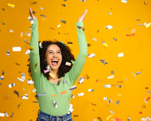 Studio Shot Of Excited Woman Celebrating Big Win Showered In Tinsel Confetti On Yellow Background