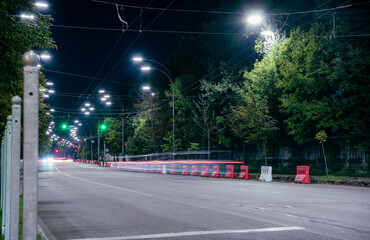 City highway at night. Green trees, lanterns illuminating the road in the night city. Crossing for pedestrians. Cars drive on the highway at night.