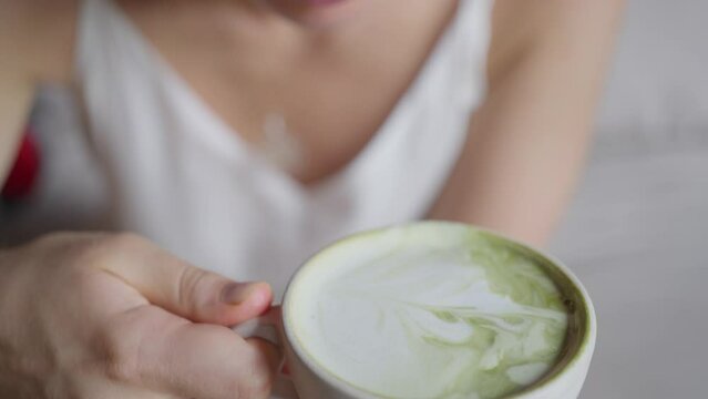 A woman drinks a green matcha latte, close-up, from a coffee cup, slow motion. Close-up. Hot green tea drink