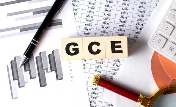 GCE text on wooden block on graph background with pen and magnifier