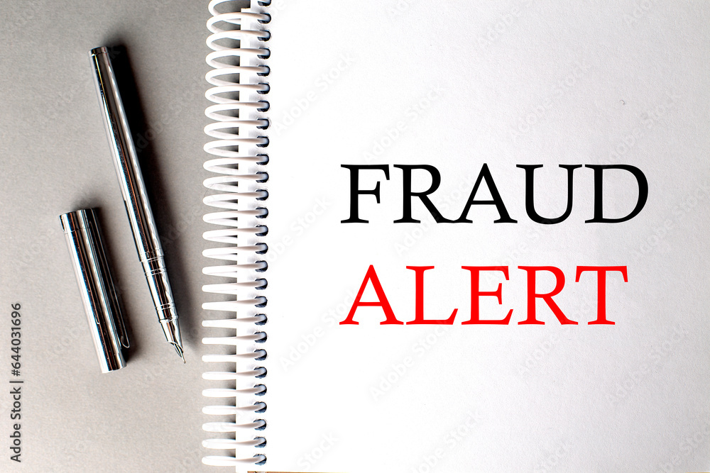 Poster fraud alert text on a notebook with pen on grey background