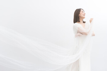 Fototapeta na wymiar 白いドレスを着た美しいアジア人女性/白いベールを風に靡かせている