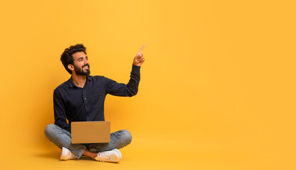 Online Offer. Smiling indian man with laptop pointing at copy space