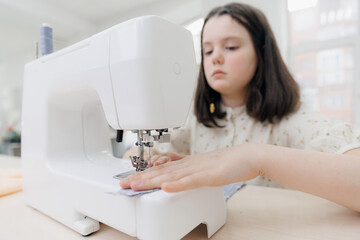 Little girl learns to sew, working with modern sewing machine on seamstress master class in school