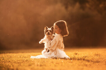 Sitting on the grass. Cute little girl is on the field with dog