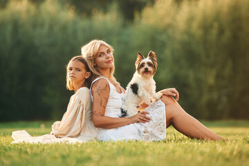 Mother with her daughter and cute dog are on the field outdoors