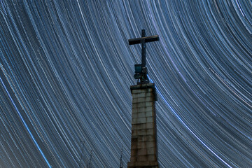 Old stone catholic cross against starry long exposure sky