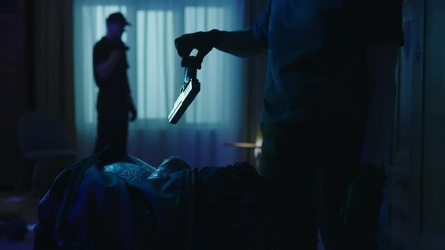 Closeup shot of black sport bag, police woman takes out the illegal objects, man with flashlight in the background. Crime scene creative concept.