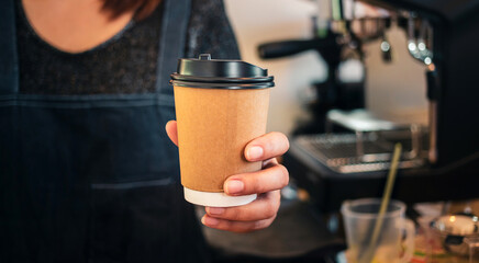 Fototapeta na wymiar Close-up of hand Barista is holding in hands hot coffee in a takeaway paper cup. Coffee take away at cafe shop, Startup successful small business concept