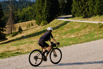Fototapeta premium Female cyclist is riding on a gravel road with a mountain view. The athlete is wearing full cycling gear and training for a cycling competition. Cycling gravel adventure in Romania.Bucegi Natural Park