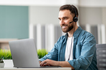 Call center operator. Handsome male manager wearing headset and typing on laptop