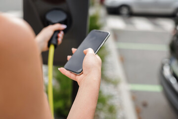 Girl connecting her electric car and a charging station with a cable charger and pressing a start button to activate a charging session